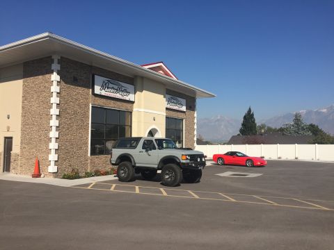 1988 Ford Bronco - A lifted, gray 1988 Ford Bronco is parked in front of a building with a "Master Muffler" sign. A red convertible is parked in the backgroun…