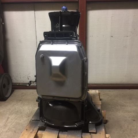 1982 Ford Bronco - A black and silver transmission assembly is shown mounted on a wooden pallet. The transmission has a large, silver pan with a dark, ribbed…