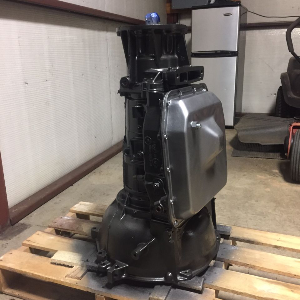 Black automatic transmission with silver pan on a wooden pallet.