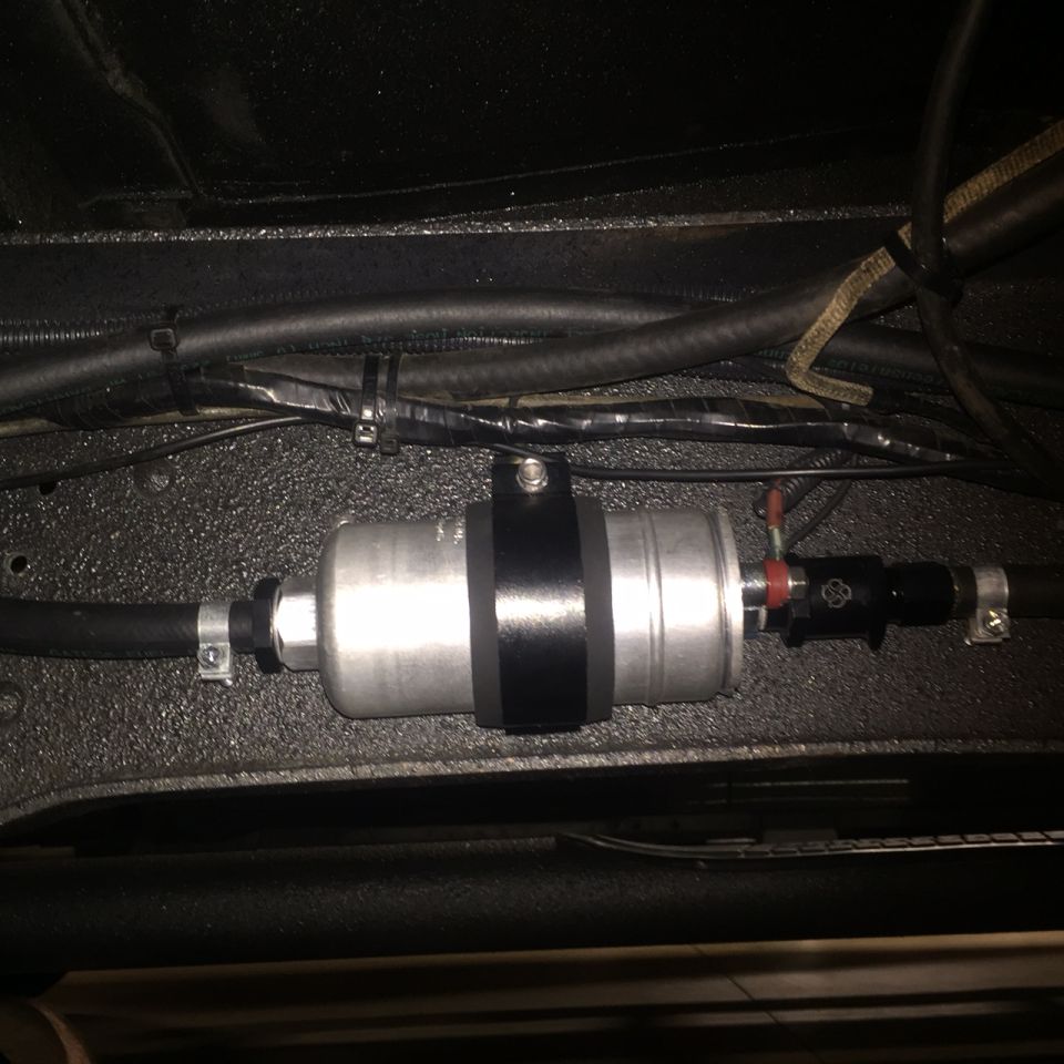 Silver fuel filter with black bands and hoses mounted to vehicle underside.