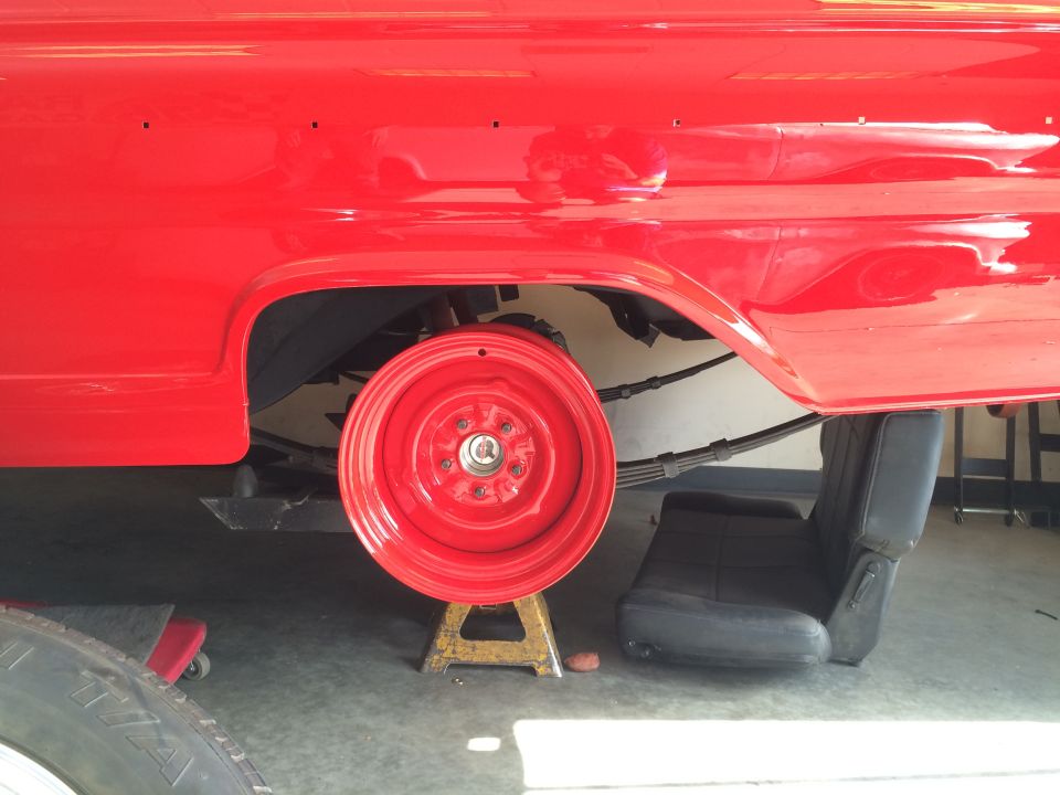 Red vintage vehicle on jack stand, red wheel removed, black seat underneath.