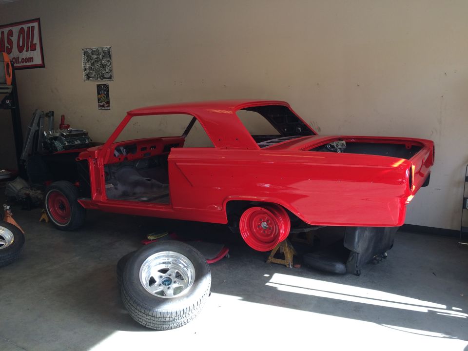 Red 1964 Ford Fairlane coupe in a garage, undergoing restoration.