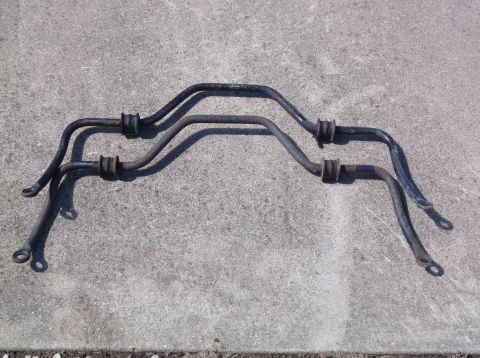 1999 Mercury Grand Marquis - Two black sway bars with rubber bushings are laid out on a concrete surface. The sway bars have a curved shape with mounting points at the…