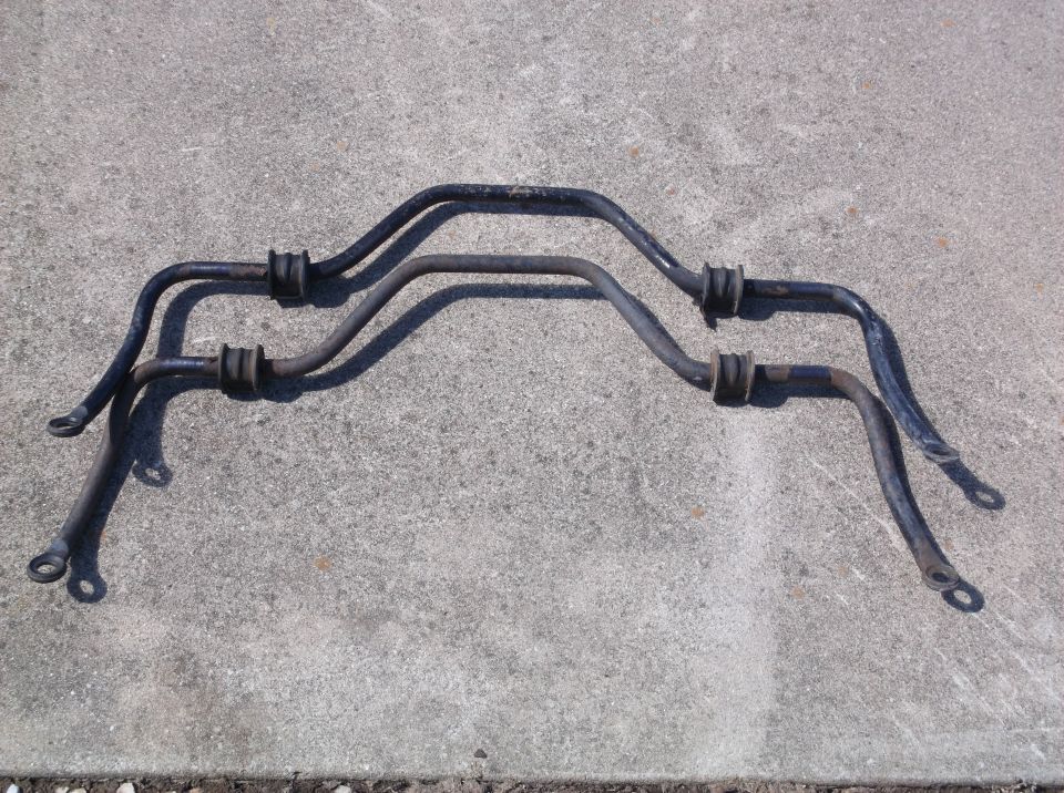 Two black sway bars with rubber bushings on a concrete surface.