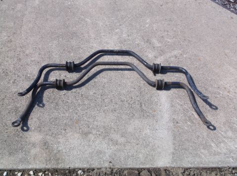 1999 Mercury Grand Marquis - Two black sway bars with rubber bushings are laid out on a concrete surface. The sway bars are curved and have mounting holes at each end.