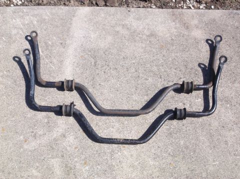 1999 Mercury Grand Marquis - Two sway bars with rubber bushings are laid out on a concrete surface. The top sway bar appears to be made of steel with some rust, while t…