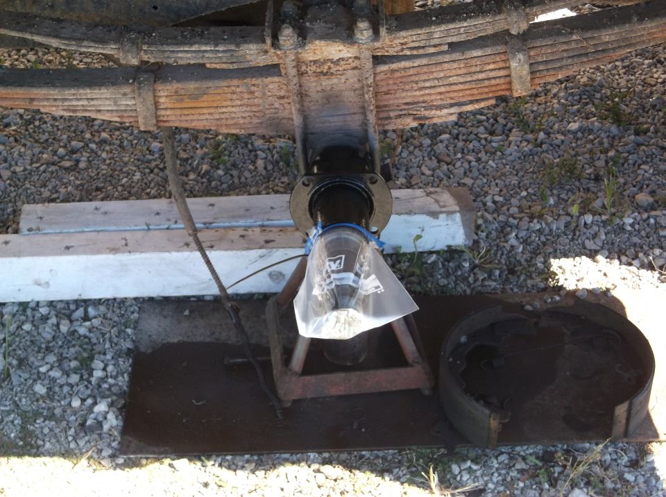 Vehicle rear axle assembly with leaf springs, brake drum, and jack stand. Fluid collection bag attached.