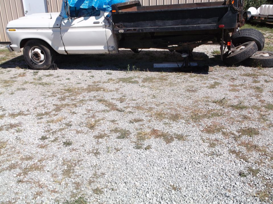 White 1970s Ford F-350 dump truck with flat front tire and rear wheels on blocks.