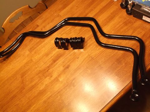 1999 Mercury Grand Marquis - Two black metal sway bars and four black sway bar brackets are laid out on a wooden table. The sway bars have a curved, symmetrical shape w…