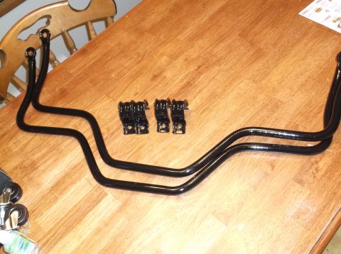 1999 Mercury Grand Marquis - Two black sway bars and four black mounting brackets are laid out on a wooden table. A portion of a wooden chair is visible in the upper le…