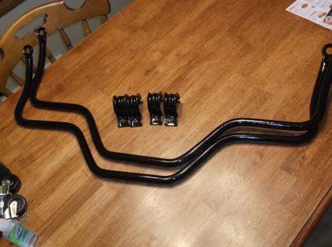 1999 Mercury Grand Marquis - Two black sway bars and four black mounting brackets are laid out on a wooden table. A portion of a wooden chair is visible in the upper le…