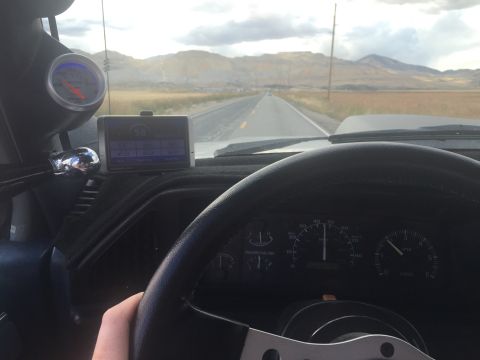 1988 Ford Bronco - Interior view of a vehicle driving on a road through a rural landscape. The dashboard shows a GPS device, a gauge, and the steering wheel w…