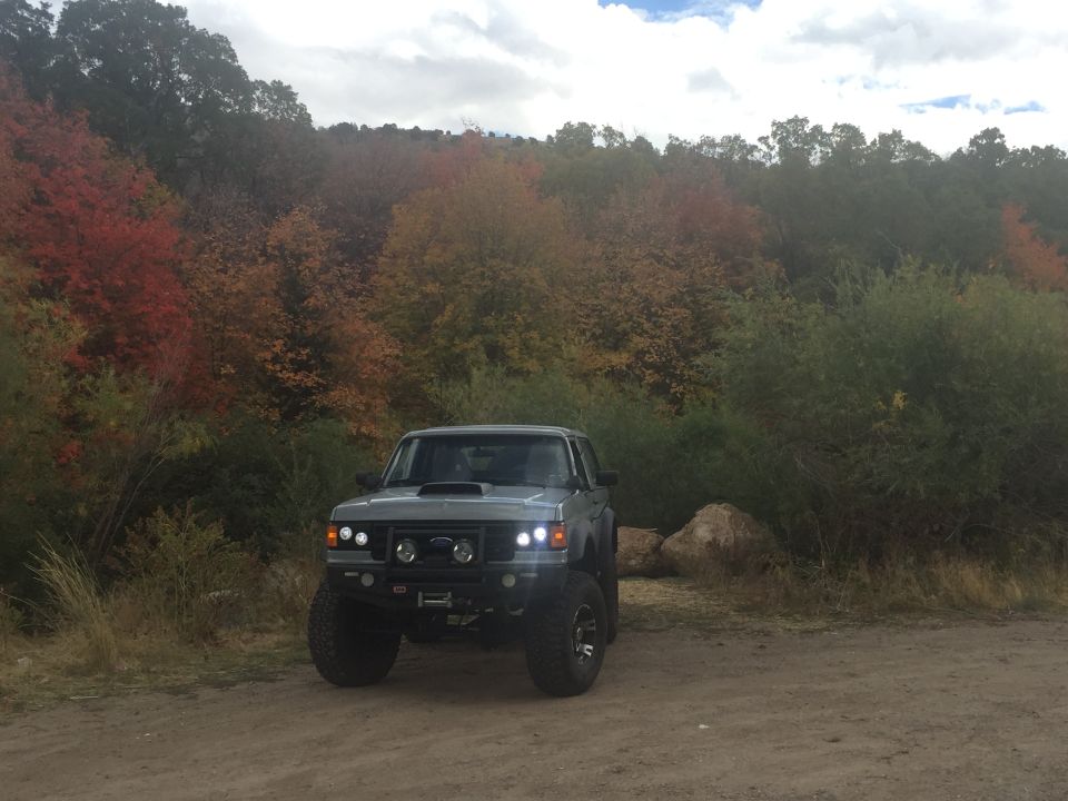 1988 Ford Bronco parked on dirt road with fall foliage in the background.