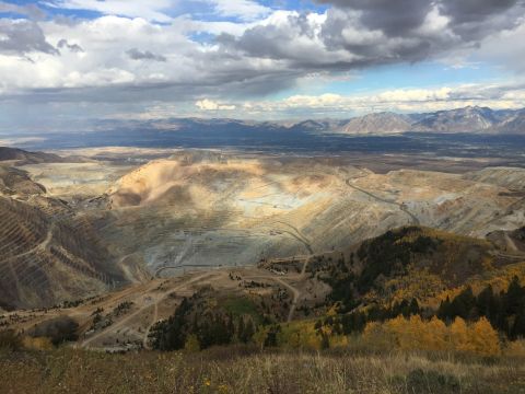 1988 Ford Bronco - A wide aerial view of a massive open-pit mine under a dramatic cloudy sky. The mine features extensive terraced excavations and roads, with…