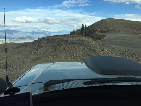 1988 Ford Bronco - View from inside a vehicle looking out at a rocky, mountainous terrain with a blue sky and clouds. The hood and windshield wipers of the ve…