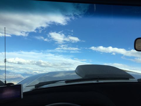 1988 Ford Bronco - View from inside a vehicle looking out the windshield at a cloudy blue sky and distant mountains. A black hood scoop is visible on the vehi…