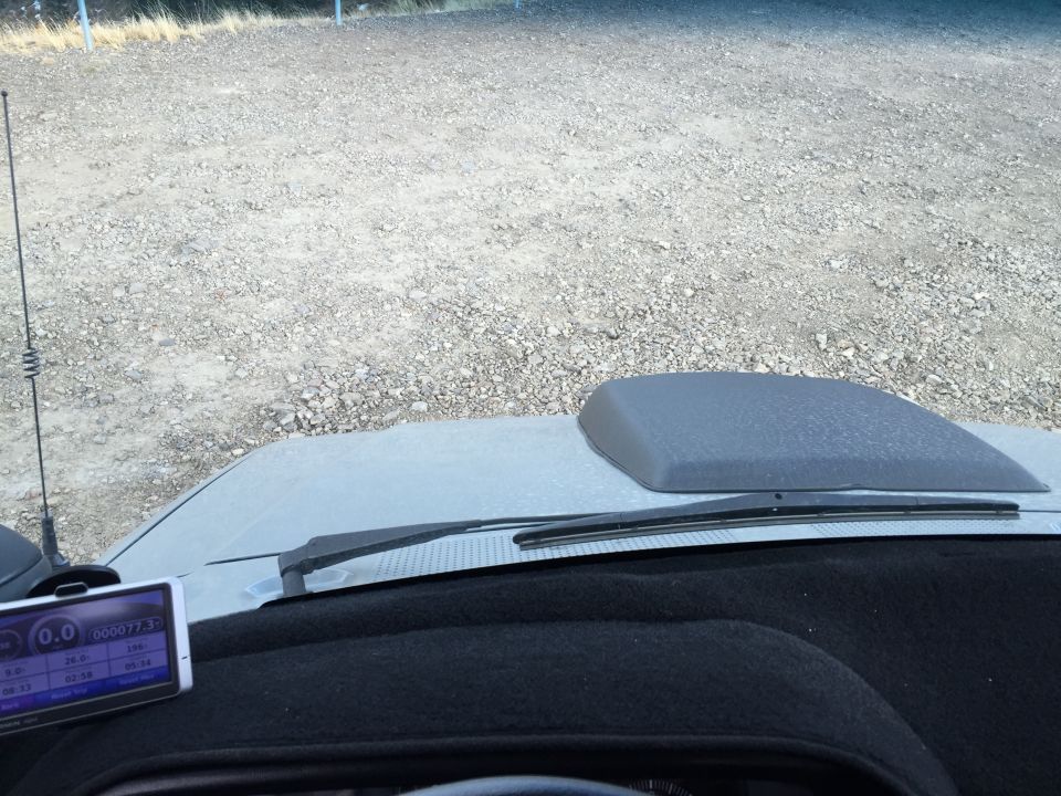 Interior view of a vehicle dashboard, hood, and GPS device with a gravel lot in the background.