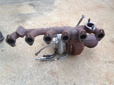 1995 Ford Bronco - A rusty turbocharger and exhaust manifold assembly is shown resting on a concrete surface. The turbocharger is a compact unit with hoses an…