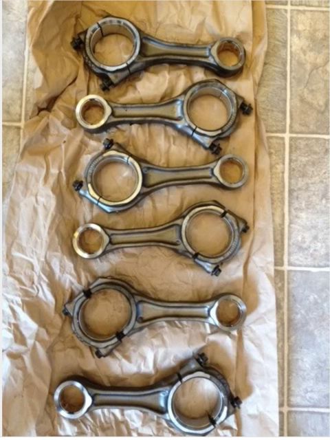 1995 Ford Bronco - A set of six connecting rods are laid out on crumpled brown paper, with a tiled floor visible in the background. The connecting rods are ma…