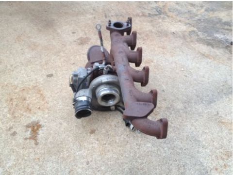 1995 Ford Bronco - A turbocharger with a cast iron exhaust manifold is shown resting on a concrete surface. The turbocharger has a silver-colored compressor h…
