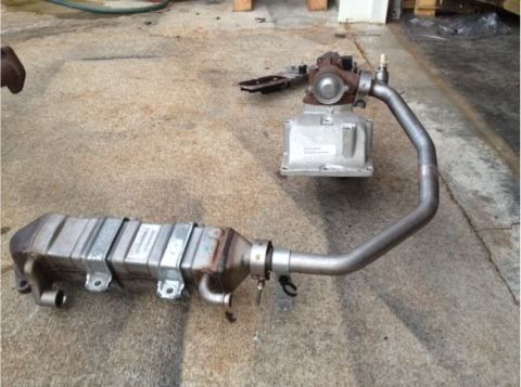 1995 Ford Bronco - A silver intercooler and exhaust pipe assembly is laid out on a concrete surface. A small metallic component with a red top is visible behi…