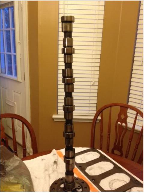 1995 Ford Bronco - A camshaft is shown standing upright on a table, with a gear attached to its base. A gasket is also visible on the table next to the camsha…