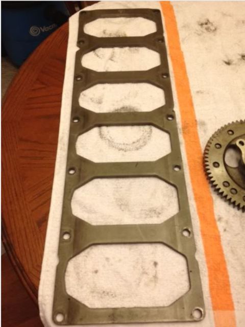 1995 Ford Bronco - A metal gasket with six oval cutouts is laid flat on a white towel with an orange stripe. A toothed metal gear is visible to the right of t…