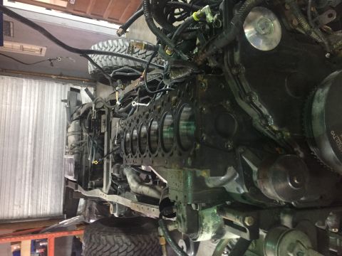1995 Ford Bronco - A close-up, angled view of a large diesel engine block with cylinders visible, surrounded by numerous hoses and wiring harnesses. The engin…