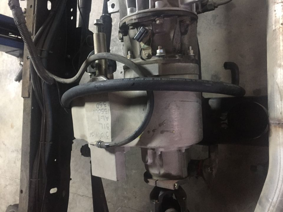 Transmission fluid reservoir with hoses and text on a vehicle.