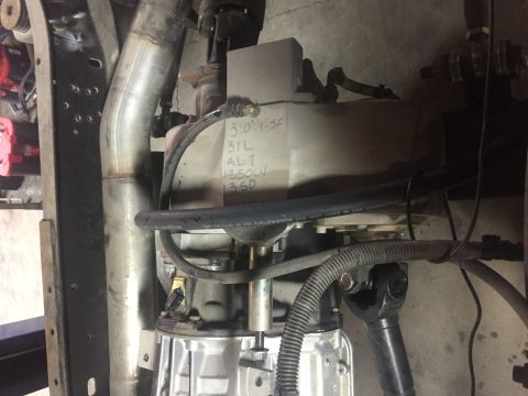 1995 Ford Bronco - A close-up view of a vehicle's drivetrain components, including a transmission, exhaust pipe, and driveshaft. Handwritten text on a grey bo…