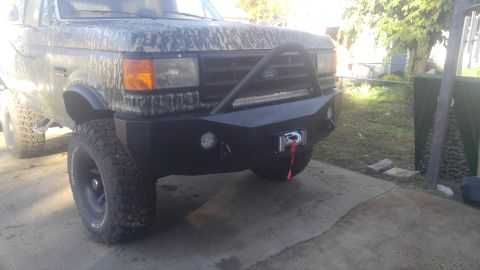 1991 Ford Bronco - A front 3/4 view of a modified Ford Bronco with a camouflage wrap, aftermarket bumper, winch, and LED light bar. The vehicle is parked on a…