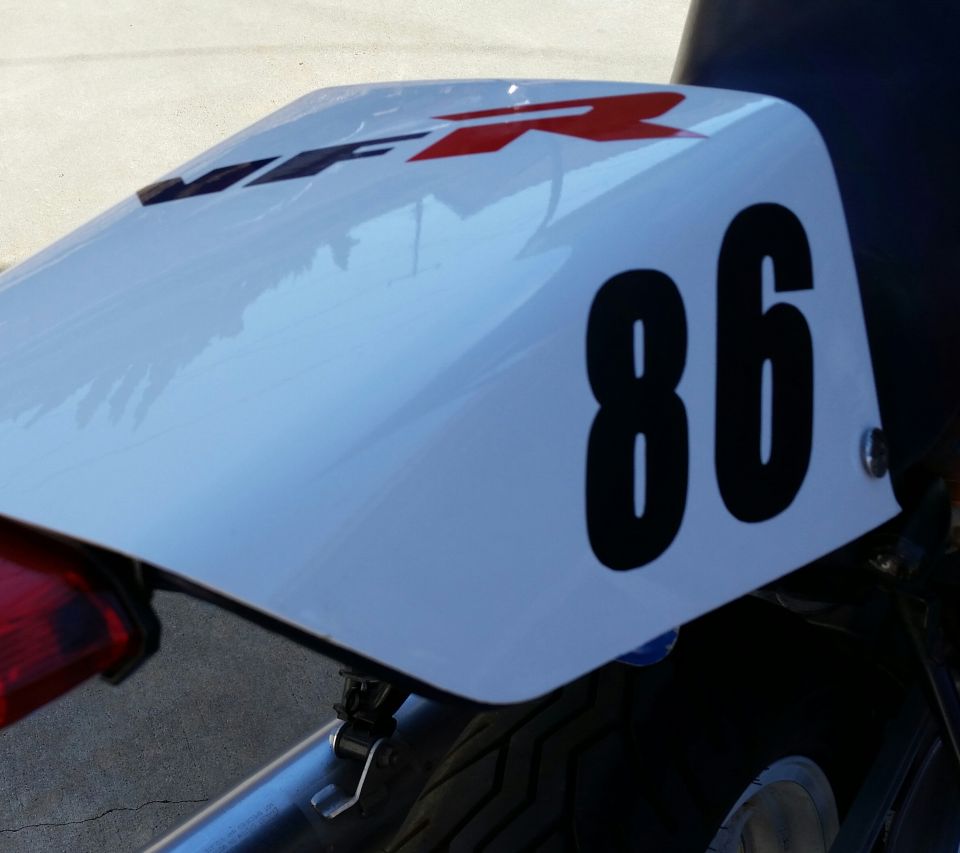 White motorcycle tail section with black number 86 and red R logo.