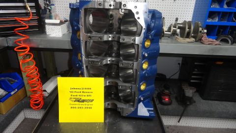 1982 Ford Bronco - A blue Ford 427w EFI engine block is displayed on a workbench next to a crankshaft. A yellow sign with information about the engine is plac…