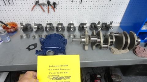 1982 Ford Bronco - A collection of engine parts, including pistons, connecting rods, a crankshaft, and a blue-painted engine component, are laid out on a work…