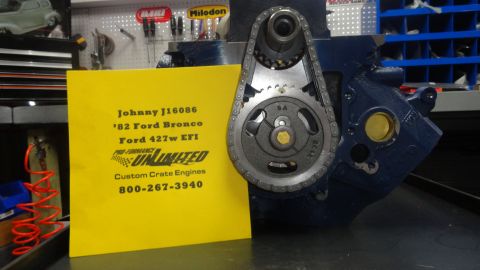 1982 Ford Bronco - A close-up of a blue engine block with a timing chain and gears is partially visible, next to a yellow sign with engine details and contact…