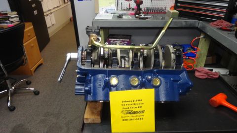 1982 Ford Bronco - A blue Ford 427w EFI engine is on a workbench, with a yellow tag detailing its specifications and contact information for "Unlimited Custom…