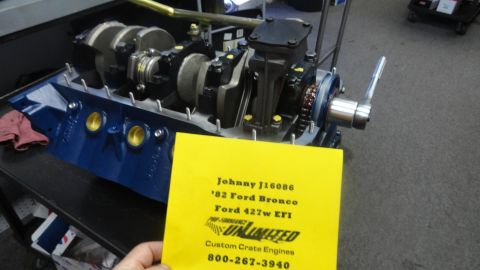 1982 Ford Bronco - A blue Ford V8 engine block with a crankshaft installed is displayed on a black stand. A yellow card with engine specifications and contact…