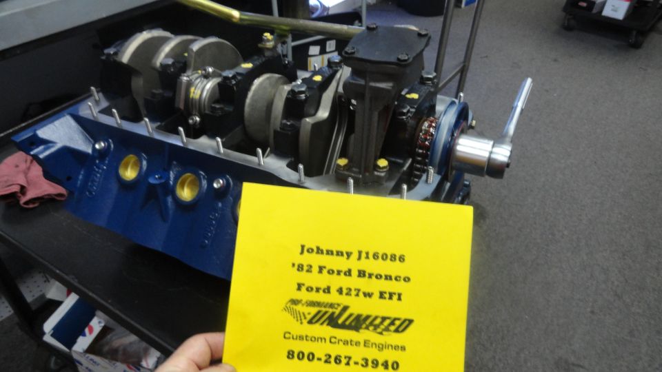 Blue Ford V8 engine block with crankshaft, on stand, with yellow spec card.