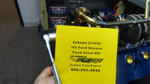 1982 Ford Bronco - A yellow card with engine details is held in front of a blue engine block. The card lists "Johnny J16086, '82 Ford Bronco, Ford 427w EFI, P…