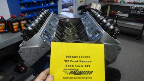 1982 Ford Bronco - A V8 engine block with cylinder heads installed is shown in a workshop setting. A yellow document with text about a '82 Ford Bronco and a F…