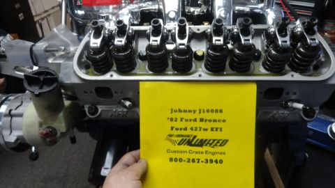 1982 Ford Bronco - A close-up view of a Ford 427w EFI engine, likely for a 1982 Ford Bronco, with a yellow informational card in the foreground. The card list…