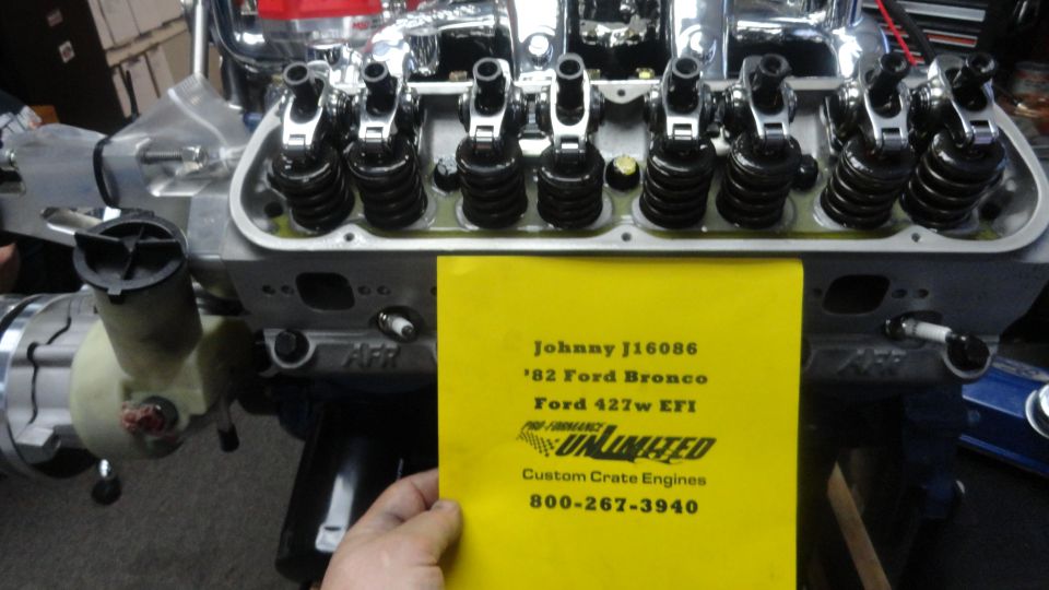 Close-up of a Ford 427w EFI engine with a yellow card listing engine details.