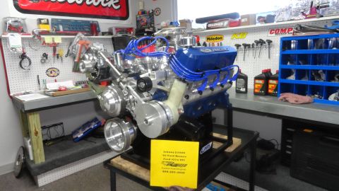1982 Ford Bronco - A custom Ford 427w EFI engine is displayed on a stand in a workshop. The engine is blue and chrome with blue spark plug wires and a yellow…