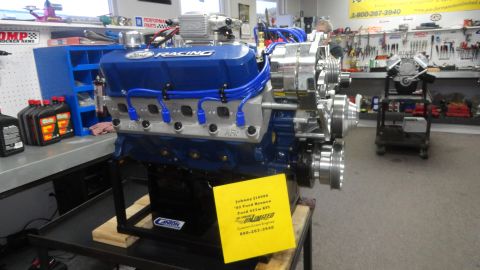 1982 Ford Bronco - A blue Ford 427W EFI engine is displayed on a stand in a workshop. A yellow sign on the engine provides details about the build.