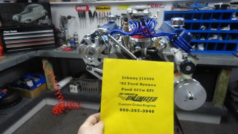 1982 Ford Bronco - A person holds a yellow document in front of a Ford 427w EFI engine. The document has text that reads "Johnny J16086 '82 Ford Bronco Ford 4…