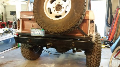 1979 Ford Bronco - The rear view of a classic Ford Bronco with a large spare tire mounted on the back. A black aftermarket bumper with a tow hitch receiver is…