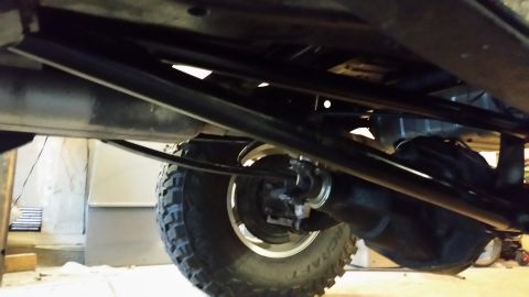 1979 Ford Bronco - Underside view of a vehicle's rear axle and suspension system, featuring large off-road tires and black metal components. The image capture…