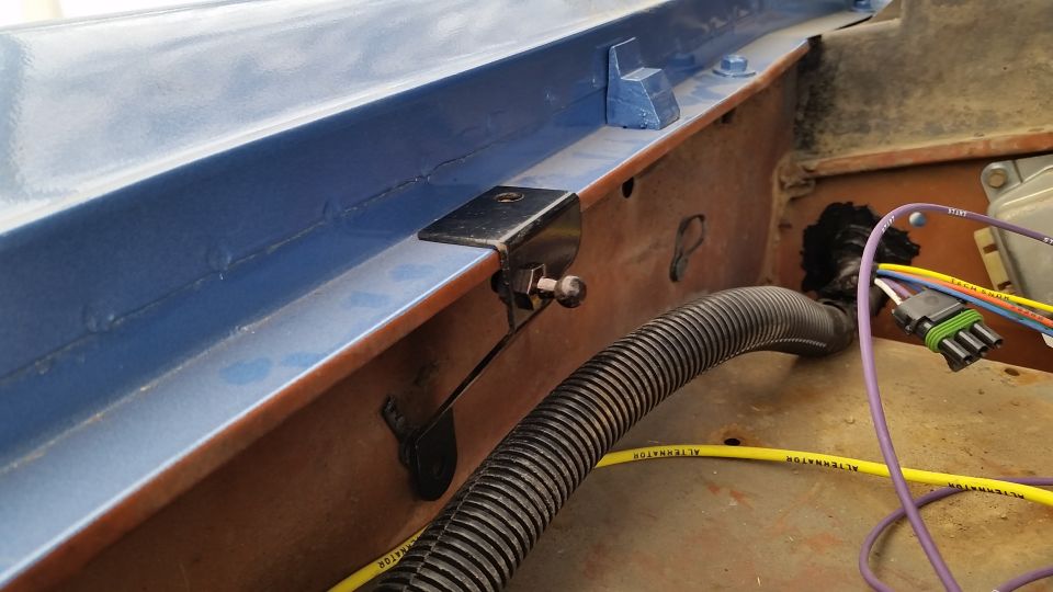 Blue-painted panel with black bracket and ball stud, wiring loom and yellow ALTERNATOR wires in engine bay