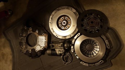 1994 Ford Bronco - A collection of automotive clutch components and a starter motor are laid out on a dark mat. Visible parts include a flywheel, clutch disc,…