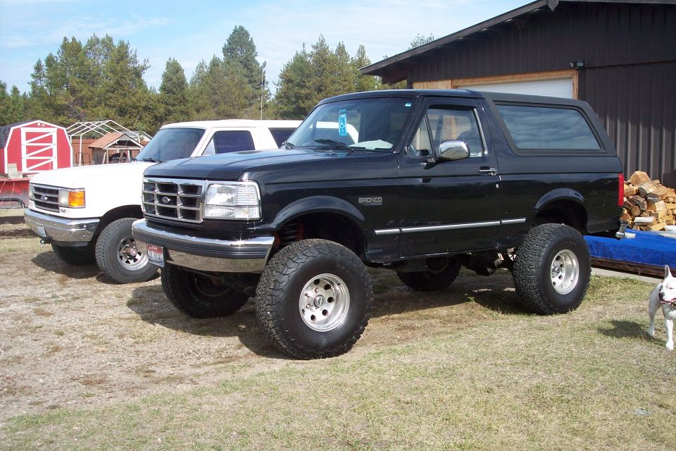 Lifted black 1995 Ford Bronco with large off-road tires parked in front of a building.